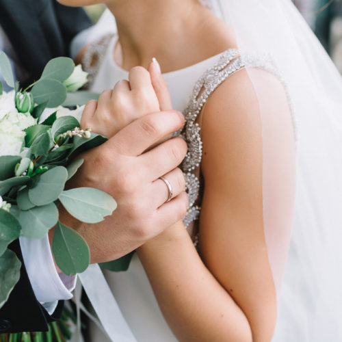 Groom holding the hand of bride with bouquet